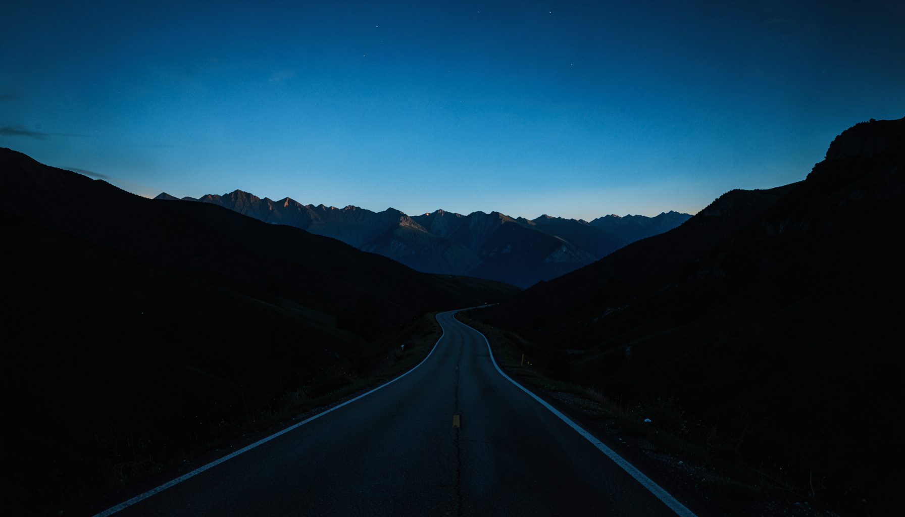 Paisagem escura e atmosférica com uma estrada sinuosa que se estende em direção a montanhas distantes sob um céu azul-petróleo
