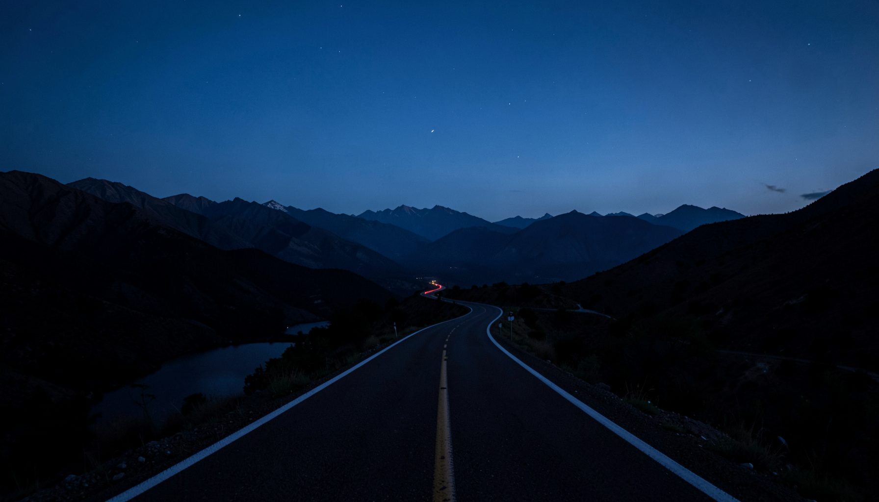 Paisagem noturna com uma estrada sinuosa estendendo-se em direção a montanhas distantes sob um céu azul-petróleo, atmosfera serena e contemplativa